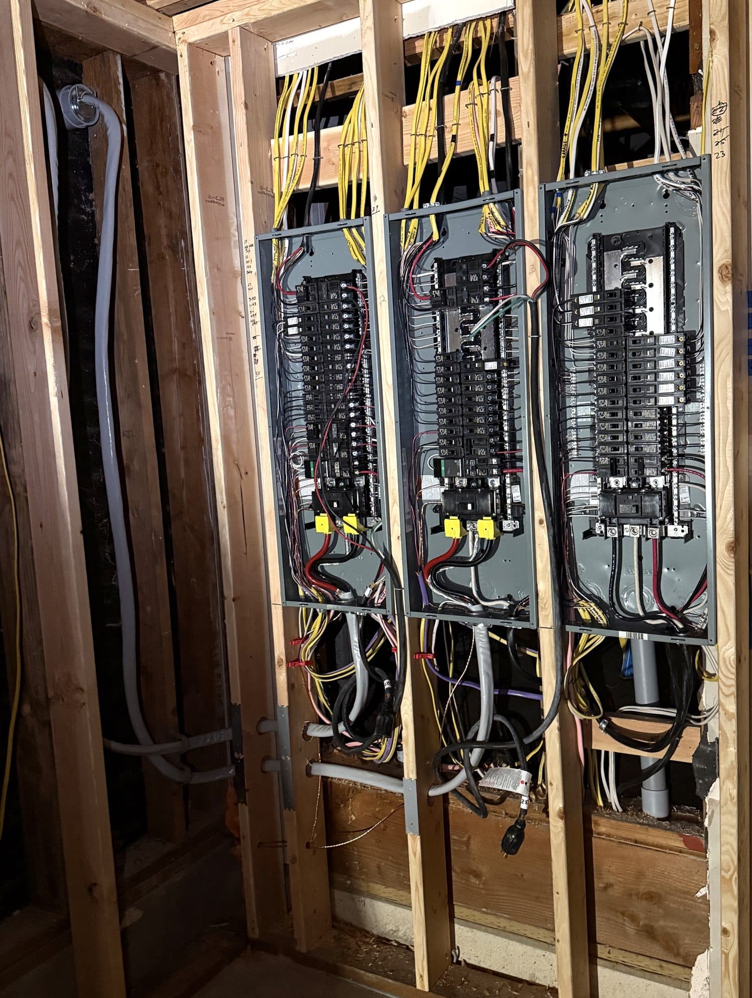 Three new electrical panels installed side by side between the studs, with the wires routed neatly into each one.