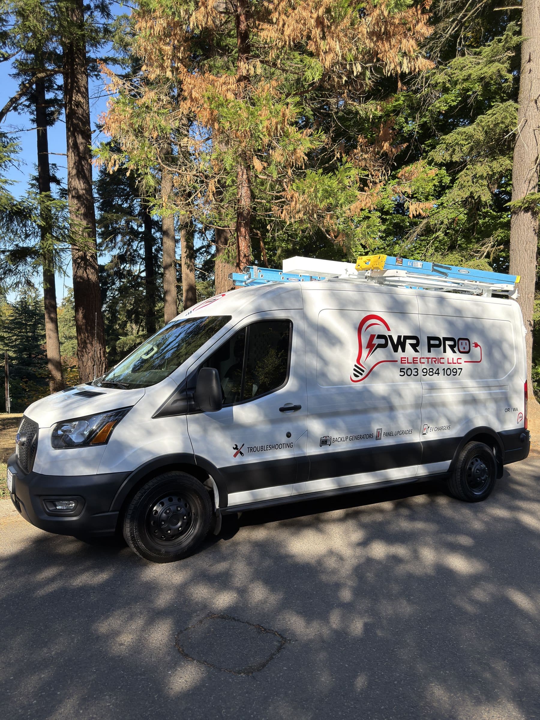 PWR Pro Electric work van with a ladder rack, parked on a road under tall fir trees