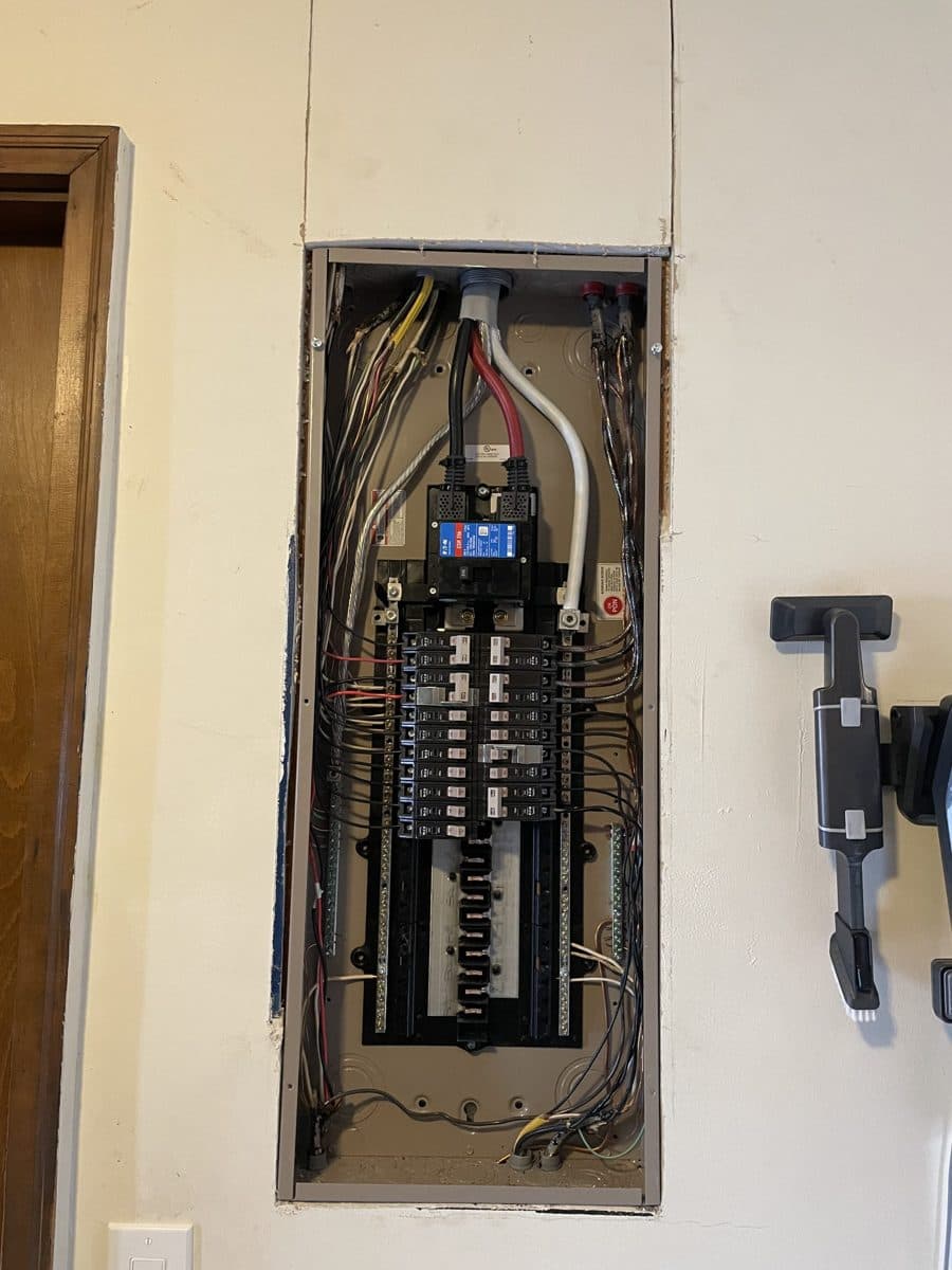 A new electrical panel set into a finished wall, with the main breaker at the top and the breakers in two neat rows.